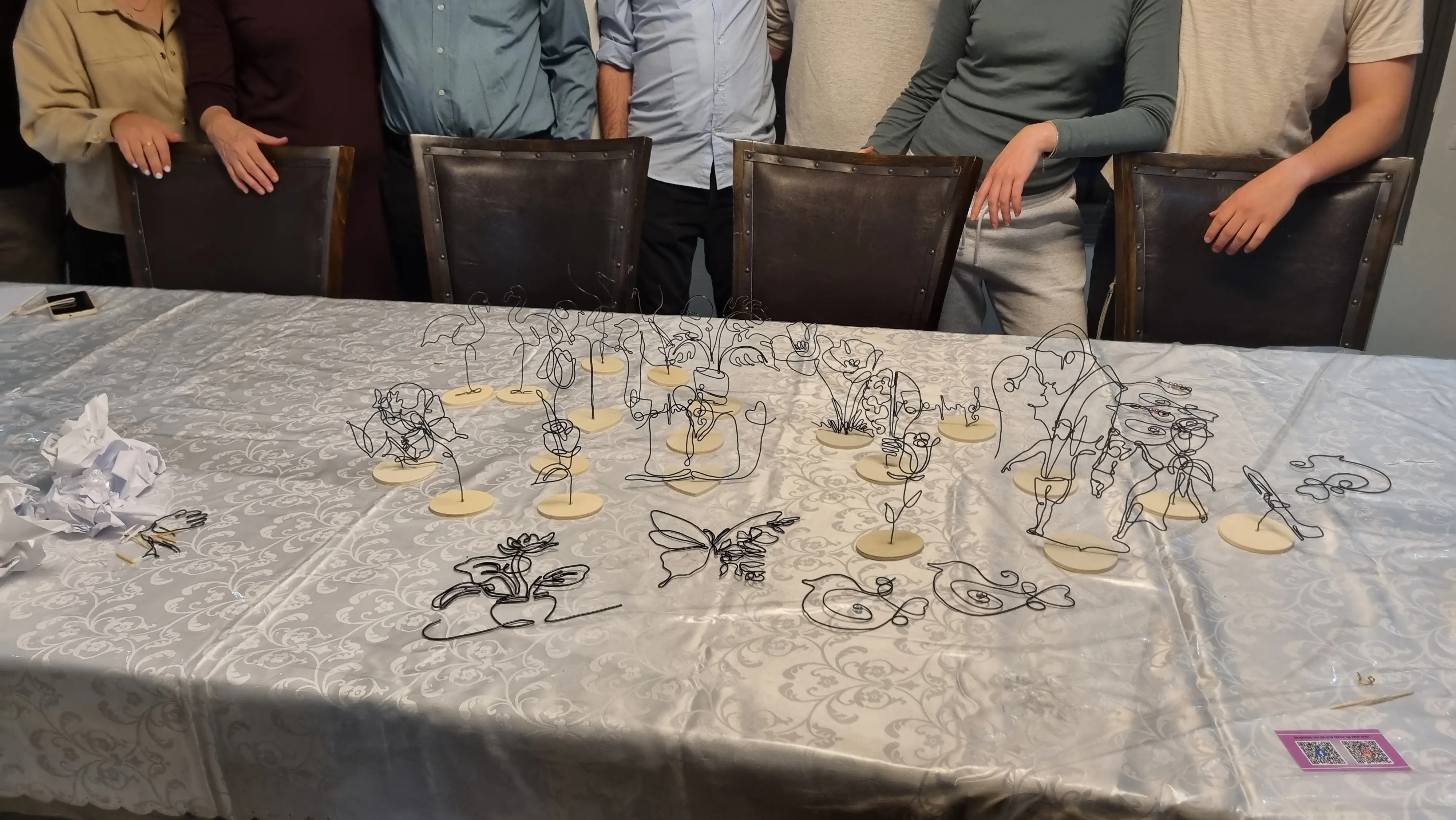 קבוצת תלמידים בשורה שמלפניהם מגוון יצירות חוטי ברזל שיצרו ,במהלך סדנא