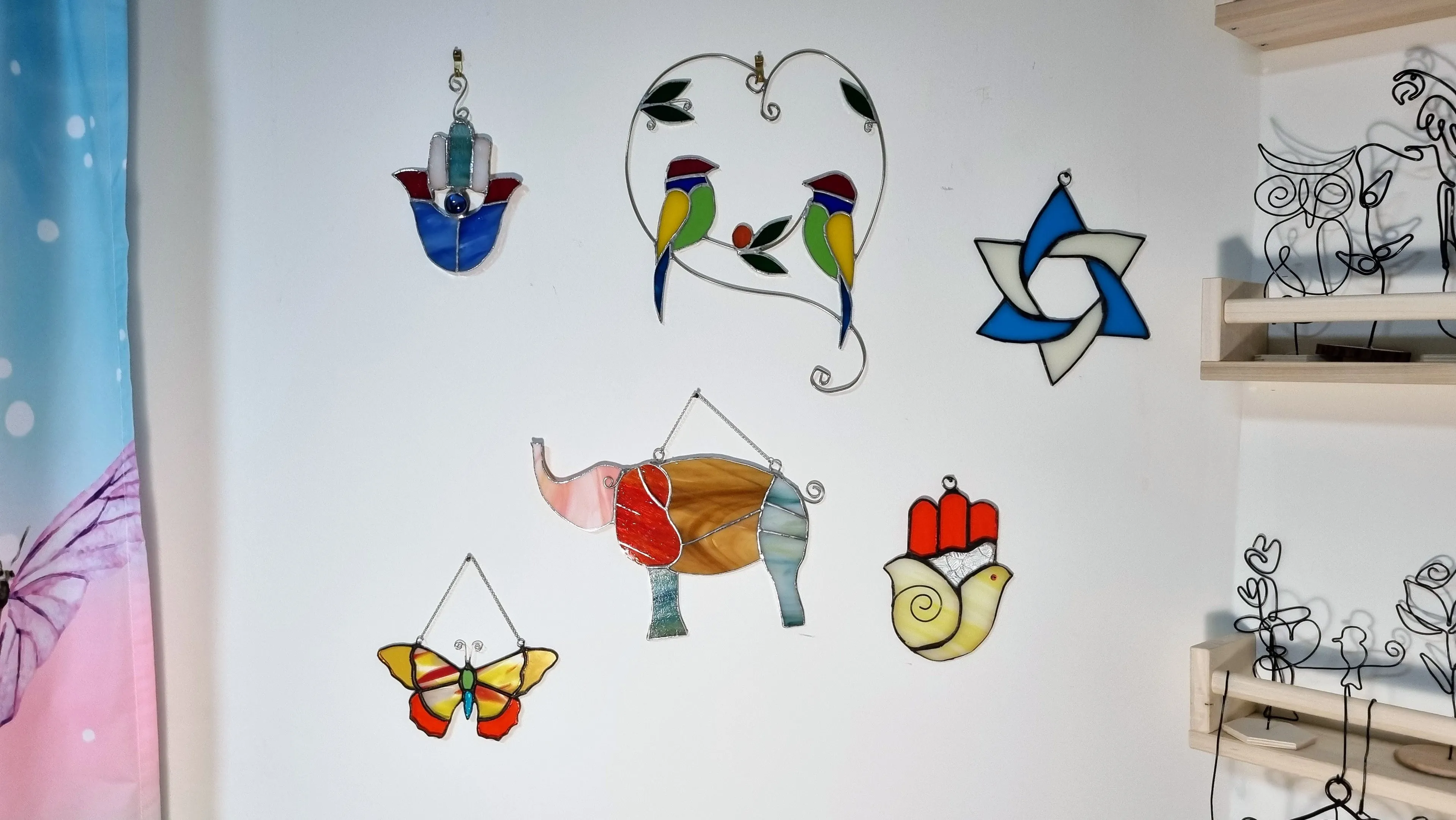 קיר בו תלויים יצירות מויטראז - חמסה, ציפורים, פיל, ועוד